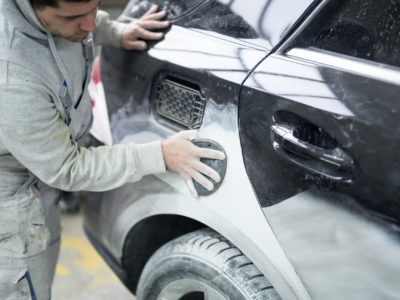 Car painter preparing car for painting in workshop.